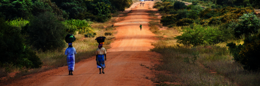 Zwei Frauen laufen auf einer breiten Straße mit Wassereimer auf den Köpfen