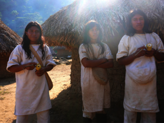 Drei Junge Kogi Männer stehen vor runden Lehmhütten in der Sierra Nevada de Santa Marta in Kolumbien